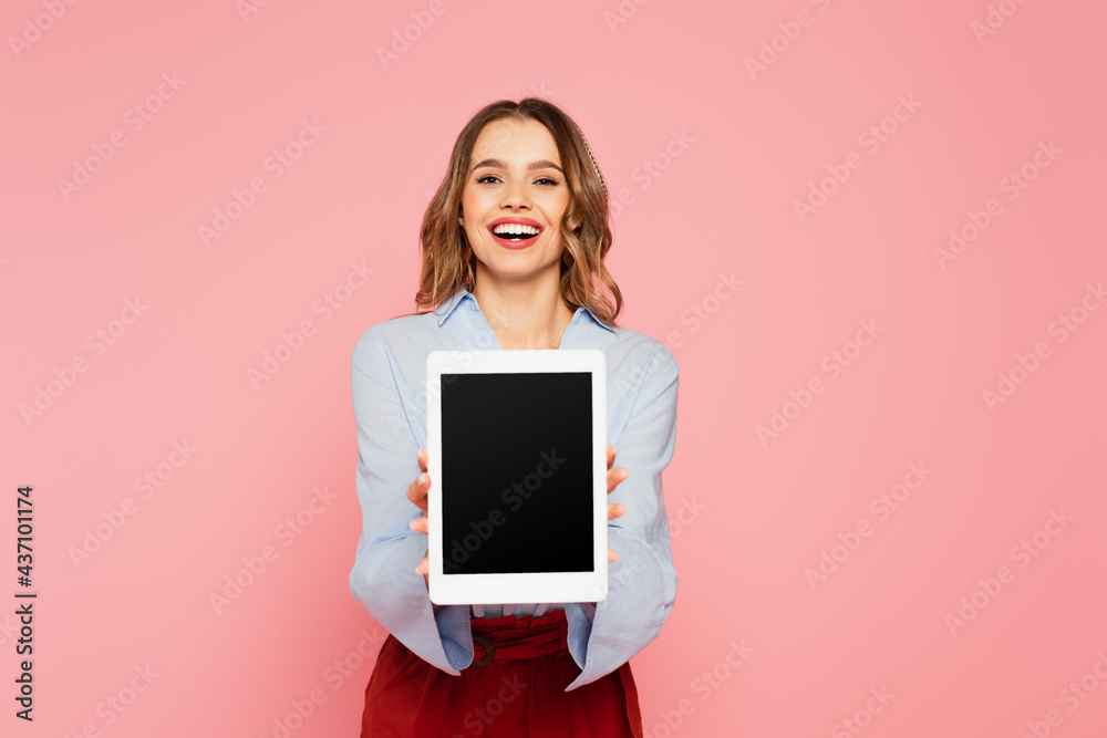 Cheerful woman showing digital tablet with blank screen on blurred foreground isolated on pink Cheerful woman showing digital tablet with blank screen on blurred foreground isolated on pink