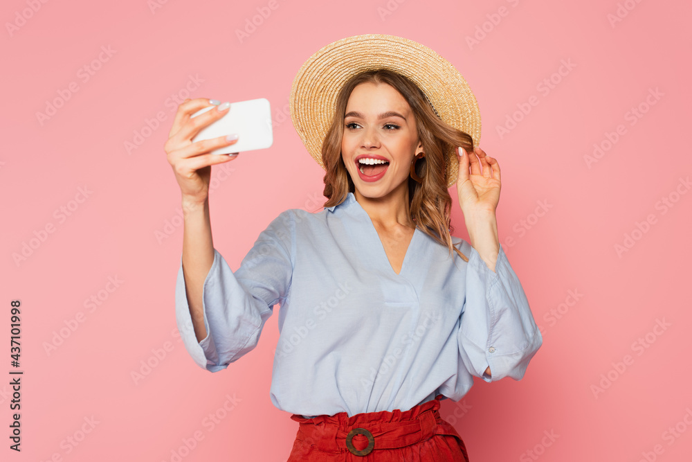 Pretty woman in summer clothes and straw hat taking selfie on smartphone on pink background Pretty woman in summer clothes and straw hat taking selfie on smartphone on pink background