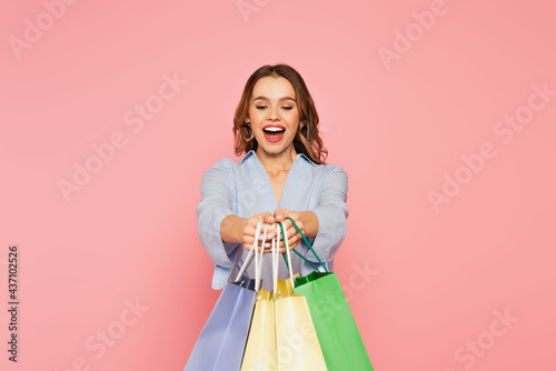 Excited shopaholic holding shopping bags isolated on pink