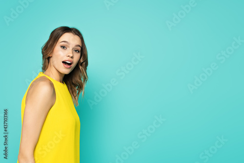 Astonished woman in yellow dress looking at camera isolated on blue