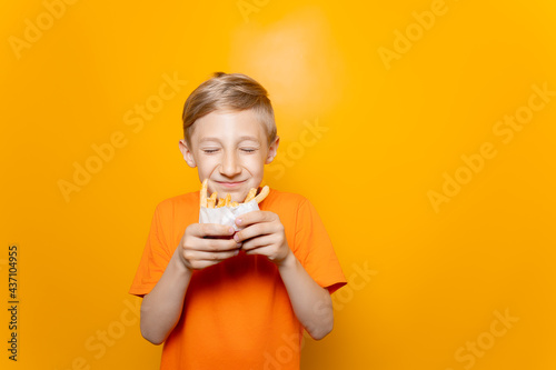 a boy in an orange T-shirt holds a bag of deep-fried potatoes in front of him and sniffs it with his eyes closed © Roman