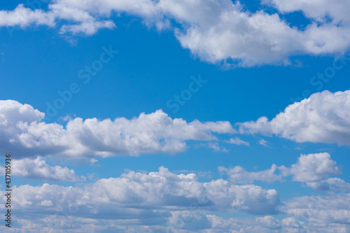 A lot of white fluffy cumulus clouds on bright summer blue sky far to horizon. Cloudscape, overcast.