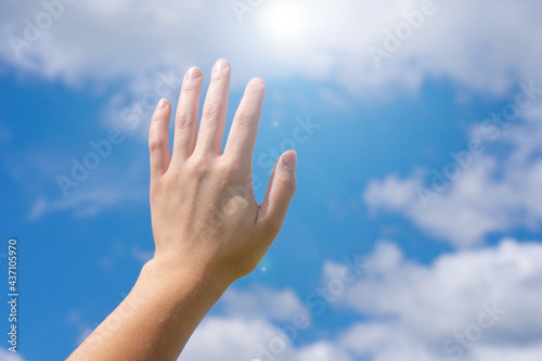 Young female hand touchs blue cloudy sky and bright sunlight.Concept of forgivness, support and inspiration.Metaphor of faith and religion, copy space photo