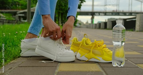 woman tying jogging shoes.A person running outdoors on a sunny day.sport girl tying shoelaces.close-up of female hands tying laces on sports shoes, before jogging a marathon, a bottle of water.USA photo