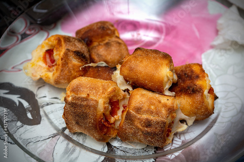 Rolls with pepperoni and cheese on a transparent plate and a colored background.