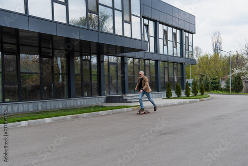 full length of middle aged man in sunglasses riding longboard outside