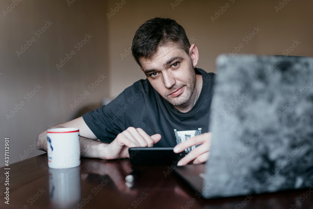 The guy at the desk with a laptop is sitting with a phone The guy at the desk with a laptop is sitting with a phone