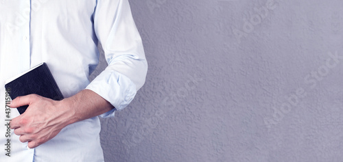 A man in a shirt holds a Bible book in his hands. On a gray background. Pastor. Prayer.