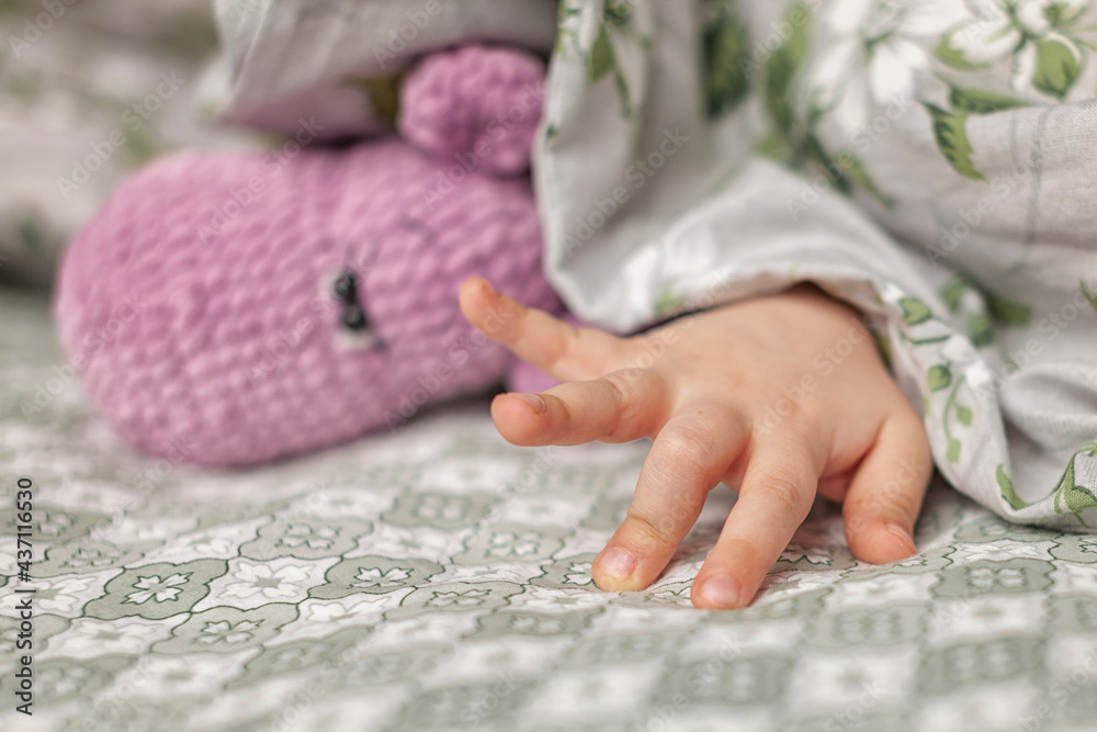child hand sticks out from under blanket, and knitted toy lies next to it