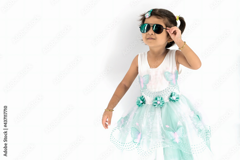 Close up of nice little indian girl with pony tail and dark sunglass , smiles and looks away, Stands over white background with copy space on the left side, Studio shot Close up of nice little indian girl with pony tail and dark sunglass , smiles and looks away, Stands over white background with copy space on the left side, Studio shot