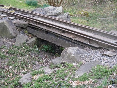 Small overpass of the track of a narrow-gauge railway over a ditch. Strong wooden planks form the bridge. The rails are heavily soiled with earth