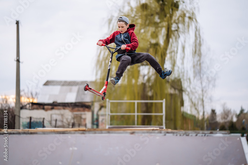 Boy on scooter makes a trick and enjoying his riding in the skate park