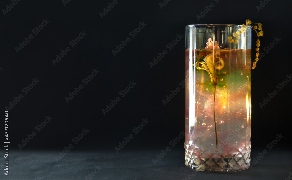 Cocktail made of natural ingredients on a black background. Composition of fresh flowers in a glass, concept