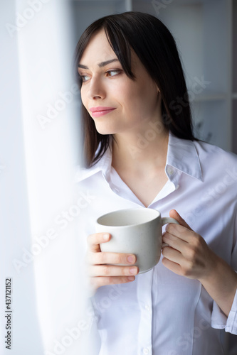 Portrait of a relaxing young beautiful brunette woman drinking coffee near the window.