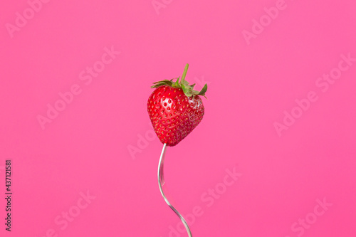 Fresh strawberries on a fork on pink background
