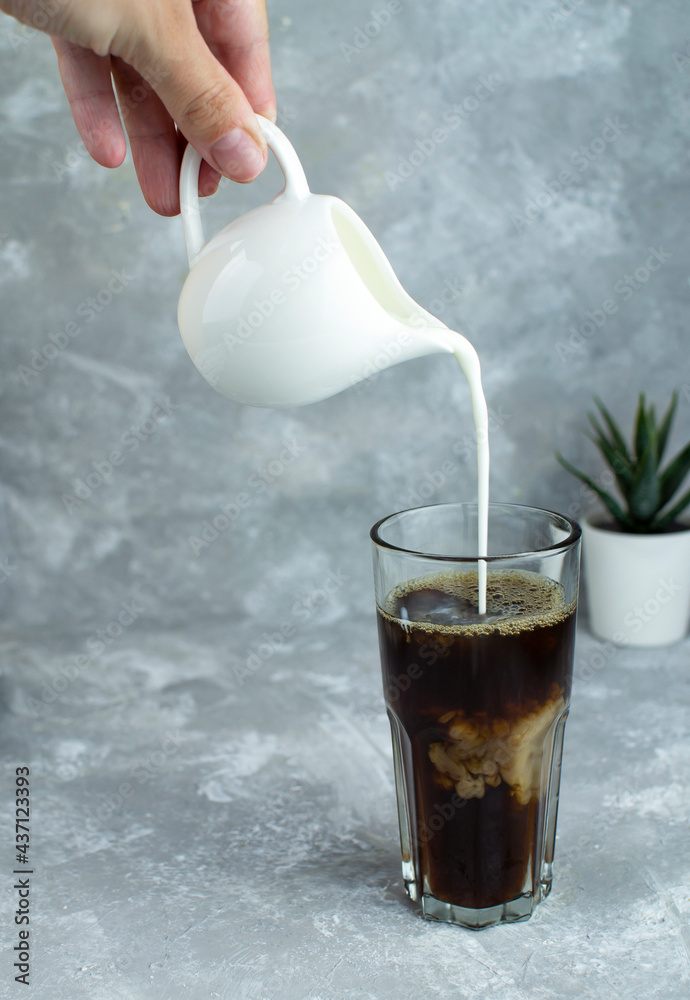 A stream of milk is poured into a glass with black coffee, creating a beautiful pattern in the drink.