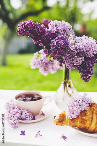 Cup of tea with lilac flowers and french croissant