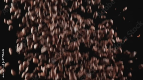 Roasted black coffee beans and a small white cup for flavorful natural coffee fly up from the bottom. The concept of natural black coffee. Black background.