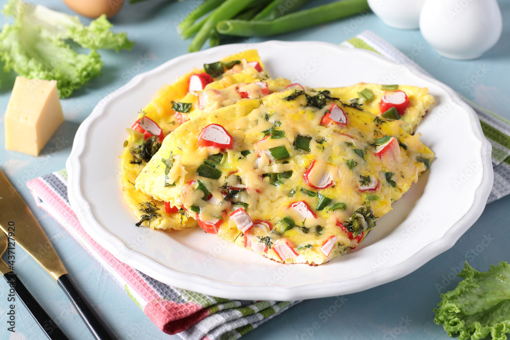 Omelet with crab sticks, cheese and green onions on a white plate on a light blue background. Closeup. Omelet with crab sticks, cheese and green onions on a white plate on a light blue background. Closeup.