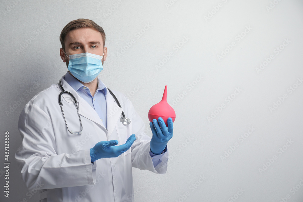 Doctor holding rubber enema on grey background. Space for text Doctor holding rubber enema on grey background. Space for text