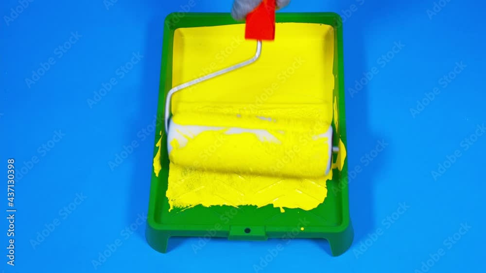 Close up of plastic tray with yellow paint on blue background. Unrecognizable person dips roller into paint. Concept of painting walls and improvement of housing conditions. Slow motion