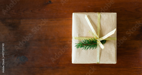Christmas gift box with Christmas tree Christmas tree branch decor and gold ribbon on a wooden brown background. Flat lay, top view with copy space. Recycled paper has been used.