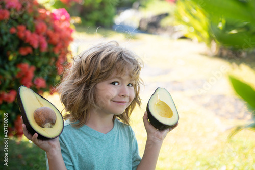 Fotomurale Close up face of kid with half an avocado in her handat tropical garden