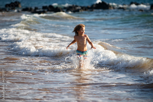 Child running through water close to shore along the sea beach. A boy runs along the sea coast. Rest of children on summer vacation.