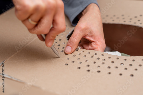 The woman punches holes in the cardboard.