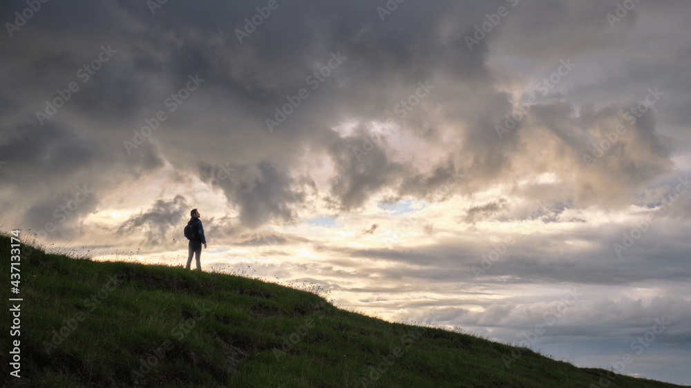 A girl walks through a meadow with plants in cloudy weather. Travel outside the