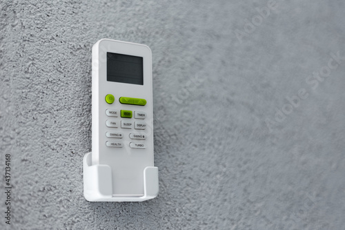 Close-up of remote control of air conditioner standing on holder, on textured wall of grey. Background with copy space.