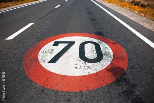 Top view of 70 km per hour, speed limit sign painted on dark asphalting road. Perspective concept.