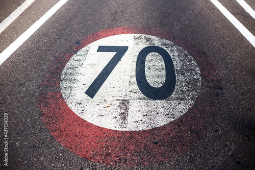 Close-up view of old shabby speed limit sign with 70 km per hour, painted on asphalting road. © Lalandrew