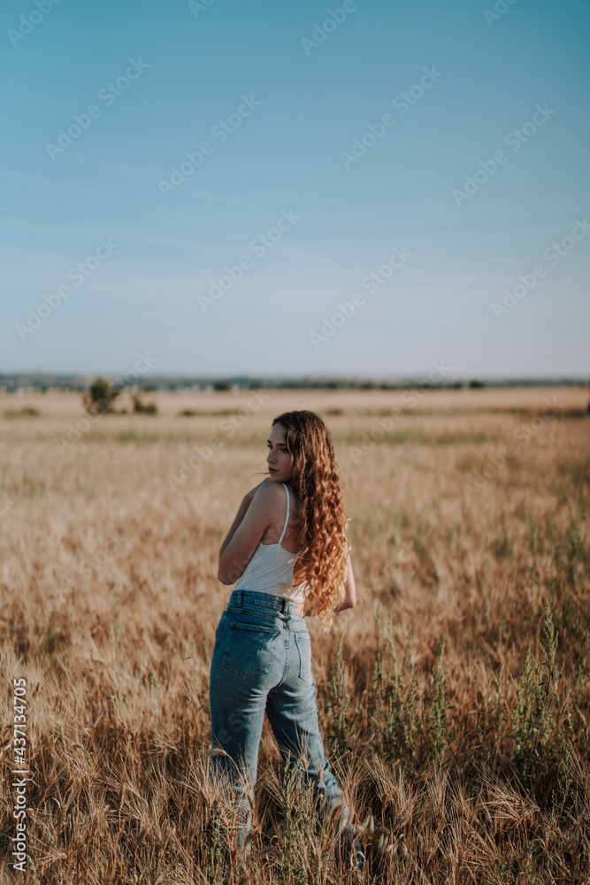 Chica joven atractiva posando en mitad de un campo de trigo al atardecer con tonos dorados