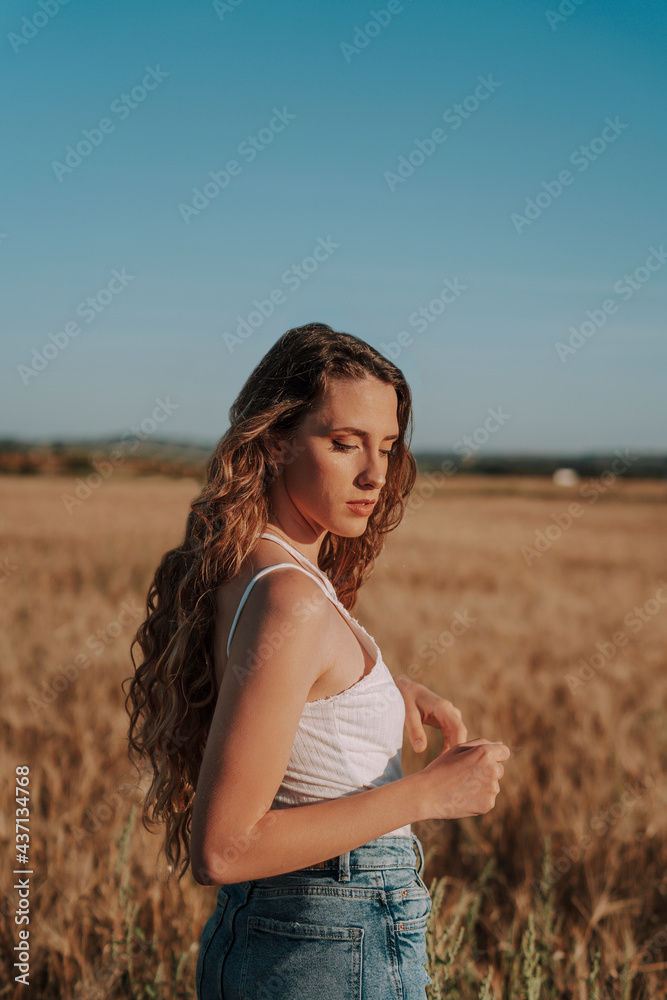 Chica joven atractiva posando en campo de trigo al atardecer con tonos dorados Chica joven atractiva posando en campo de trigo al atardecer con tonos dorados