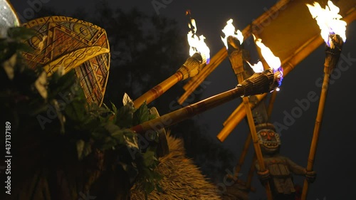 This video shows a row tiki torches held by tiki gods lining the hut of an outdoor Polynesian luau at night. photo