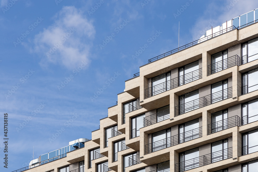 A fragment of a laconic residential high-rise building with balconies in light colors, with a blue sky in the background. Apartments in a modern skyscraper