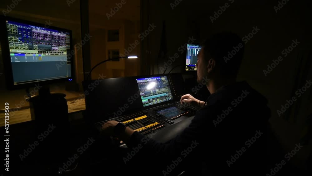Lighting engineer works on a light console in his office overlooking the theater stage. Lighting engineer works on a light console in his office overlooking the theater stage.