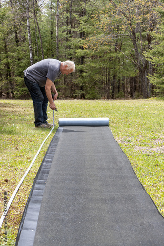 Man bending over measuring tar paper for roof