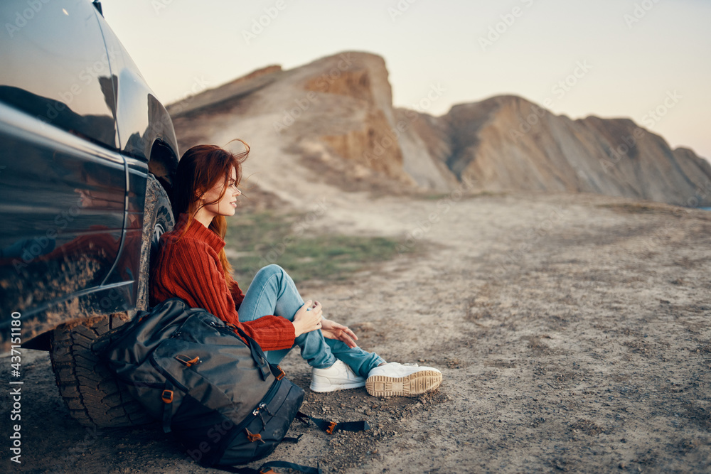 woman hiker in the mountains on nature sits near the car and mountains in the background sky road landscape