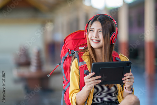 Fotografie A young traveler wears headphones and searches for a place with a tablet on the train station platform