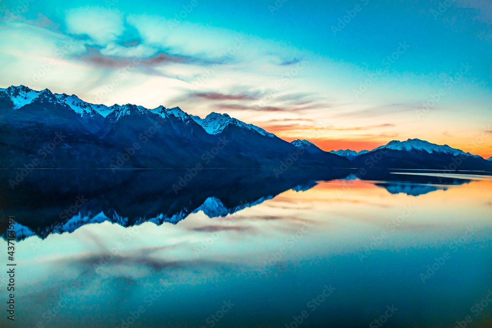 Magical vibrant sunset and red skies over Lake Wakatipu with the mountain range reflected on the calm water