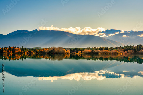 Magical vibrant sunset and red skies over Lake Wakatipu with the mountain range reflected on the calm water