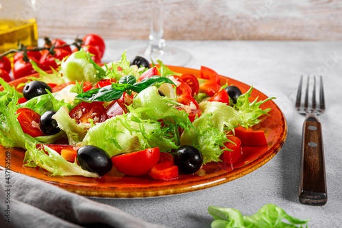  Simple summer salad of lettuce, tomatoes with olives and olive oil on a red plate close-up