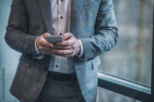 Hands of man in gray suit with smartphone