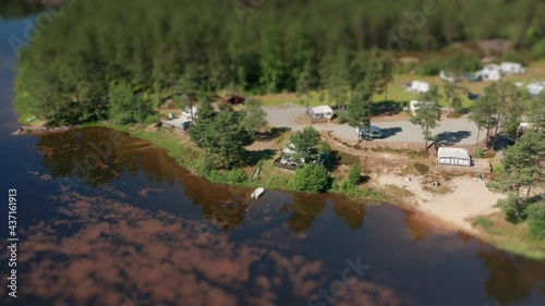 A flight above a Kilefjorden camping located nearby a coniferous forest on a coastline of Otra river. Camper vans and cars are parked freely, a lonely boat is tied with a rope to the shore. photo