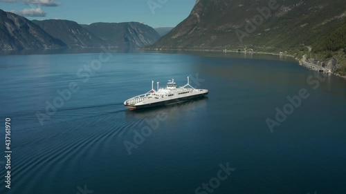 Kaupanger-Laerdal ferry crossing. An electric ferry moving fast on the still waters of the fjord nearing the harbour. Mountains, covered with pine forest rise from the water. The sky is clear. photo