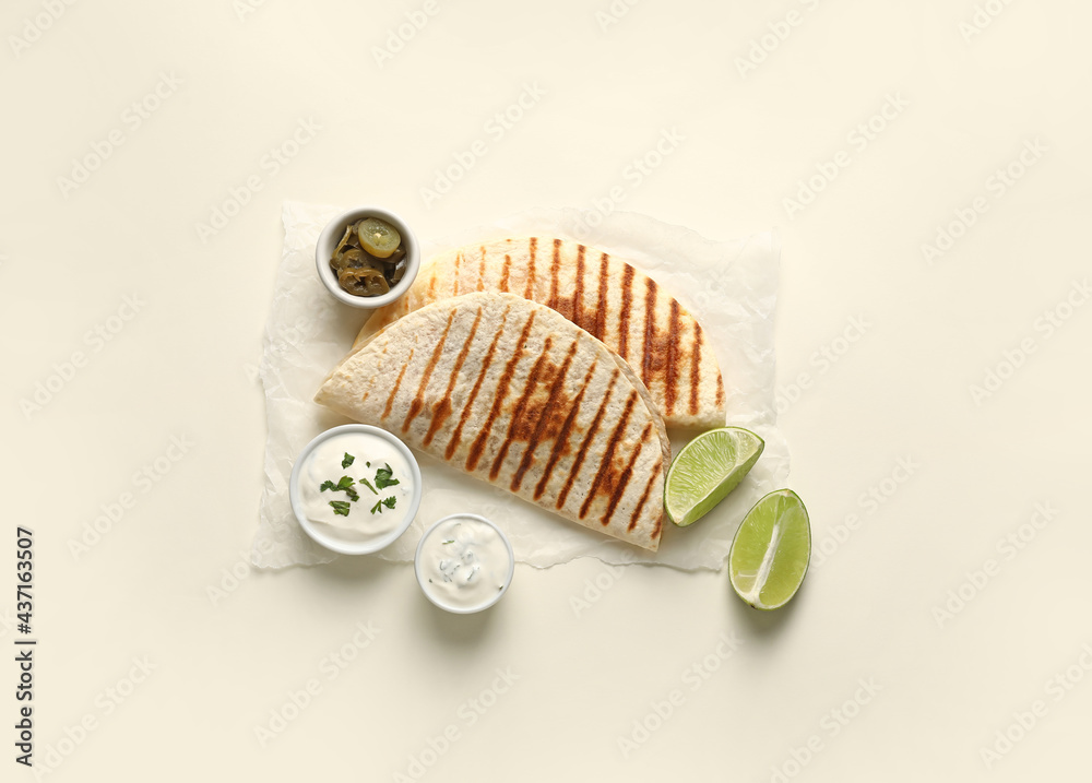 Parchment with tasty quesadillas, lime, sauces and pickled jalapenos on white background