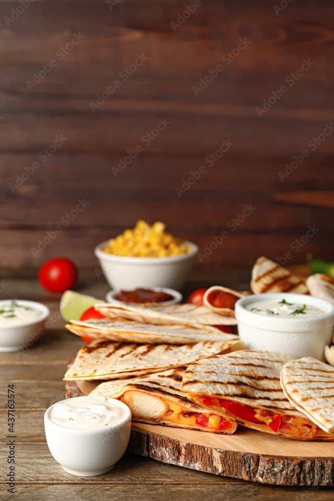 Board with tasty quesadillas, lime and sauces on wooden background