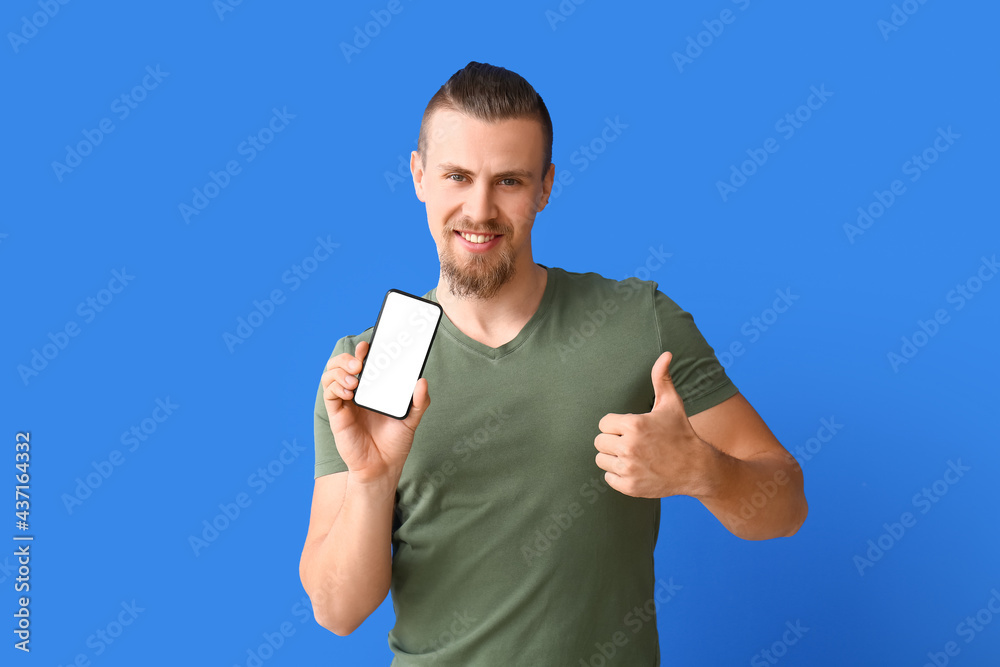 Young man with mobile phone showing thumb-up gesture on color background Young man with mobile phone showing thumb-up gesture on color background